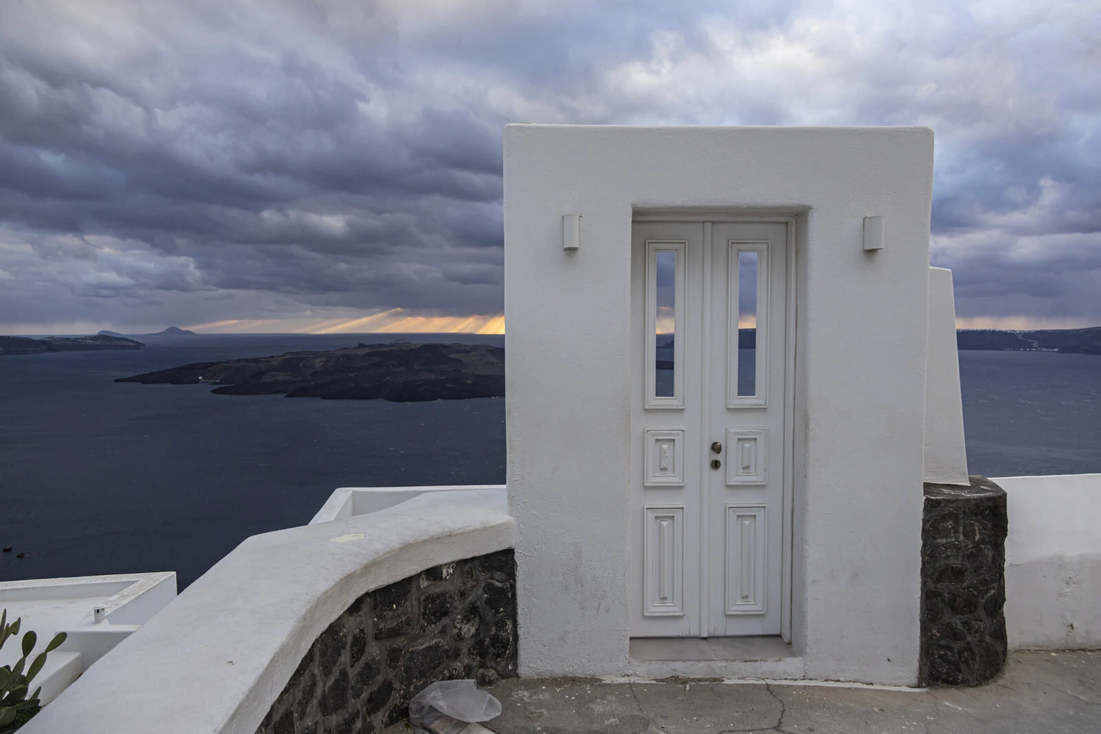 A hotel entrance in Santorini with a view of Nea Kammeni islet in the distance.