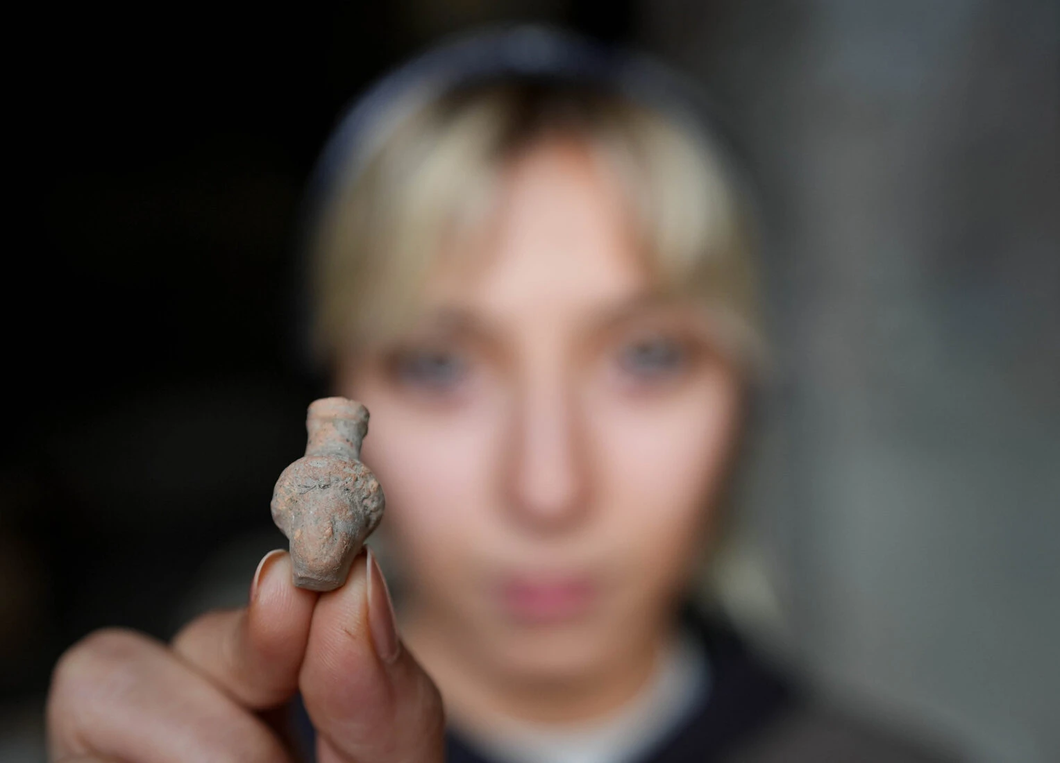 A female archaeologist displays a small artifact found at the "Mosaic House" of the Ancient City of Pergamon, Izmir, Türkiye.