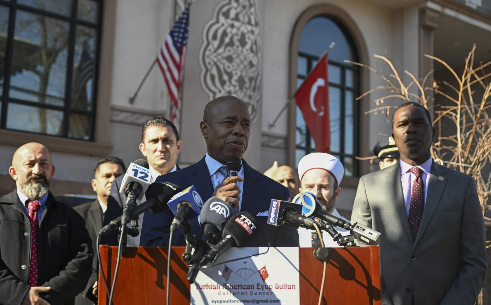 photo shows NYC mayor eric adams speaking, turkey flag on background