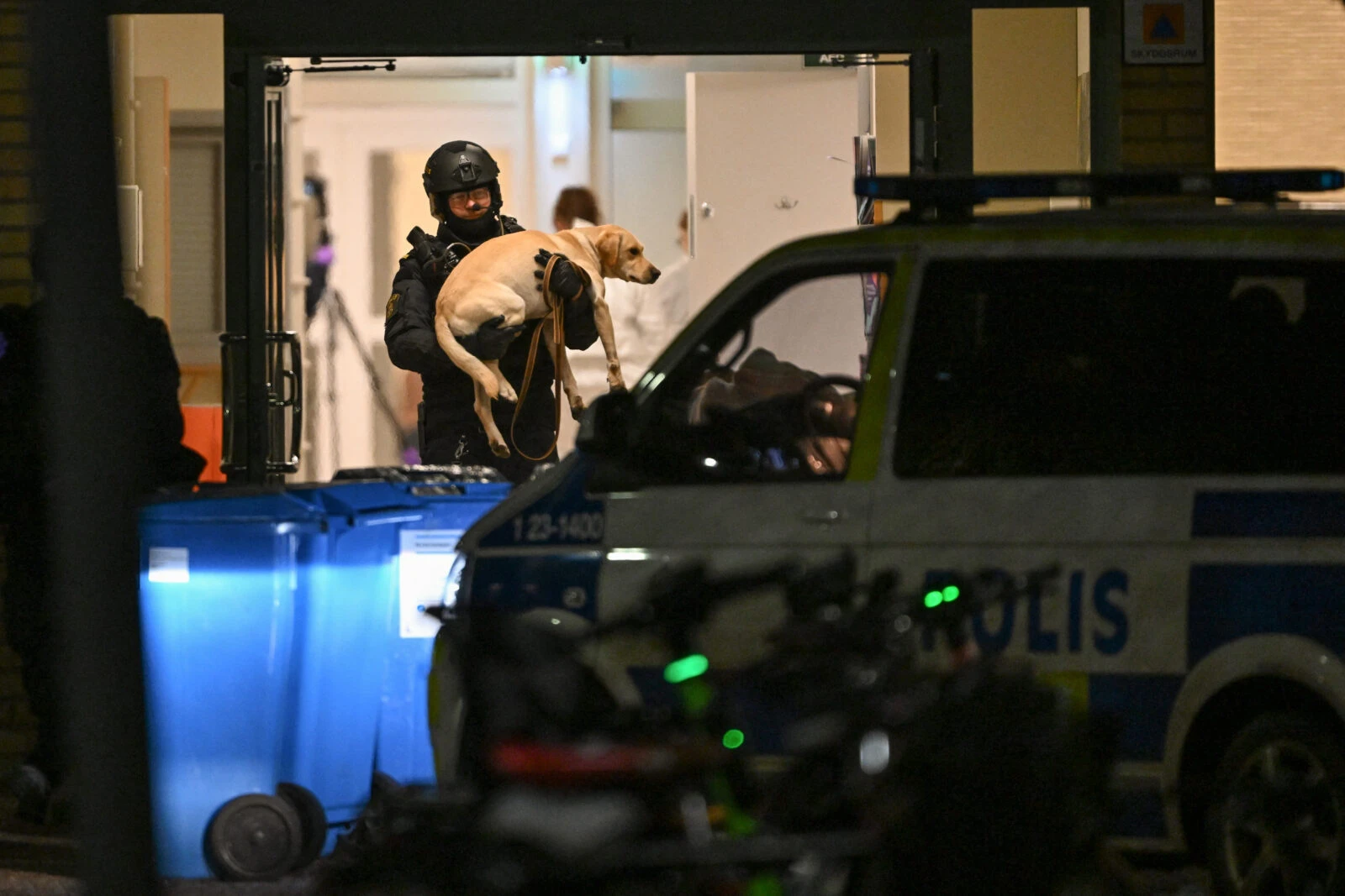 Photo shows a police officer carrying a dog.