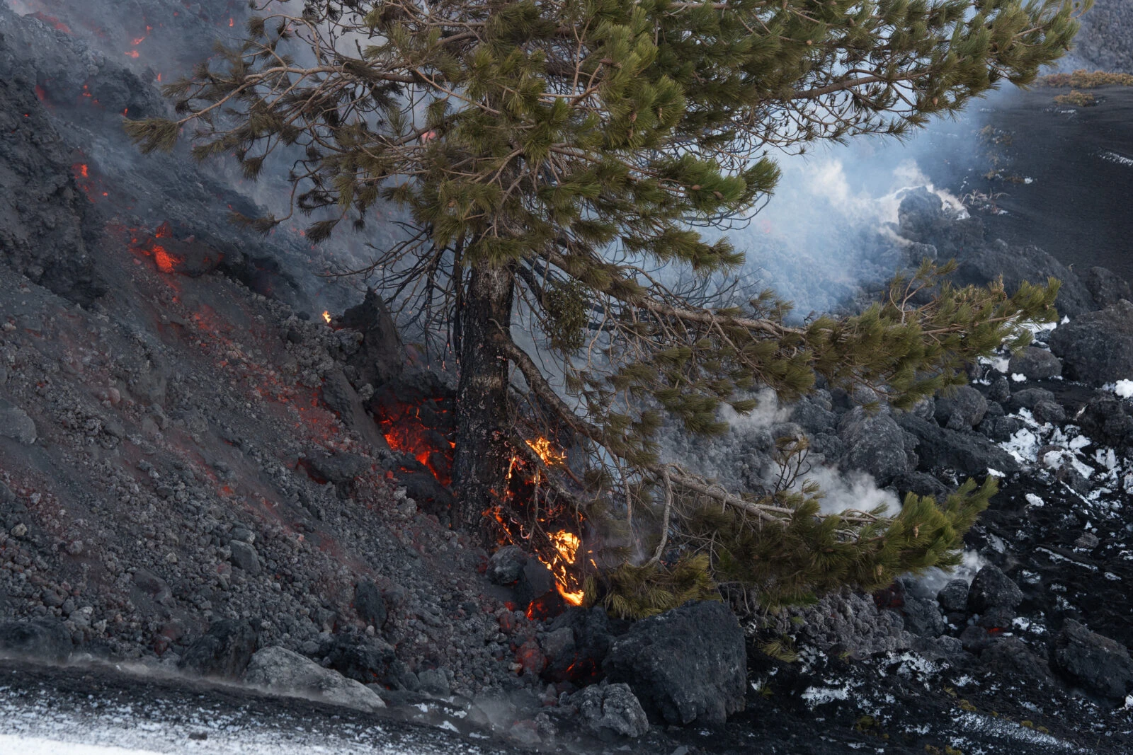 A vivid stream of molten lava flows from a fissure on Mount Etna during an eruption at night, casting a fiery glow against the dark sky.