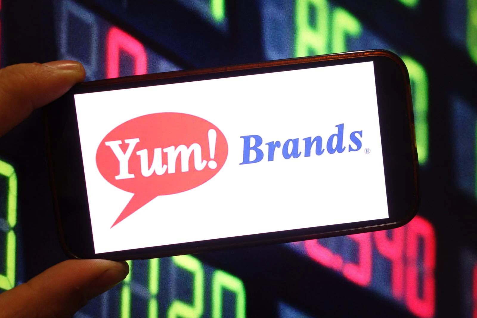 Photo shows a person holding a smartphone displaying the logo of Yum! Brands