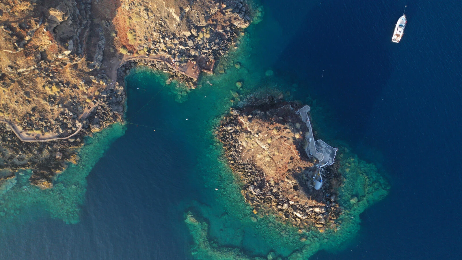 Aerial view of the volcanic islet with the Chapel of Agios Nikolaos in the bay of Amoudi, Santorini, Greece.