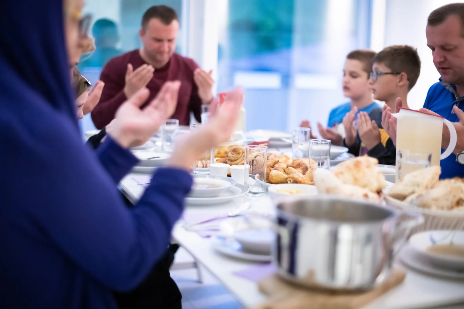 Muslim people praying before iftar and enjoying traditional food during Ramadan at home.