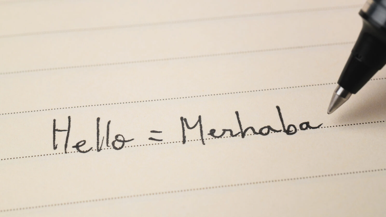 Close-up shot of a notebook with a beginner Turkish language learner writing 'Hello=Merhaba' for homework.