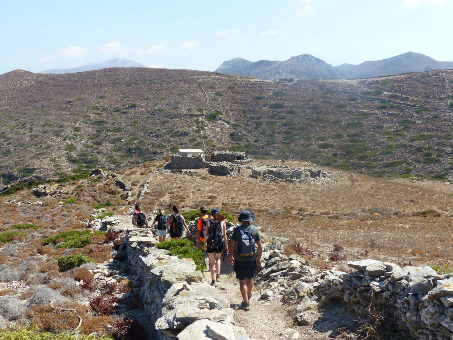 A group of hikers dressed in outdoor gear walks along a rugged nature trail in the countryside of Amorgos, a serene island in the Cyclades, Greece.