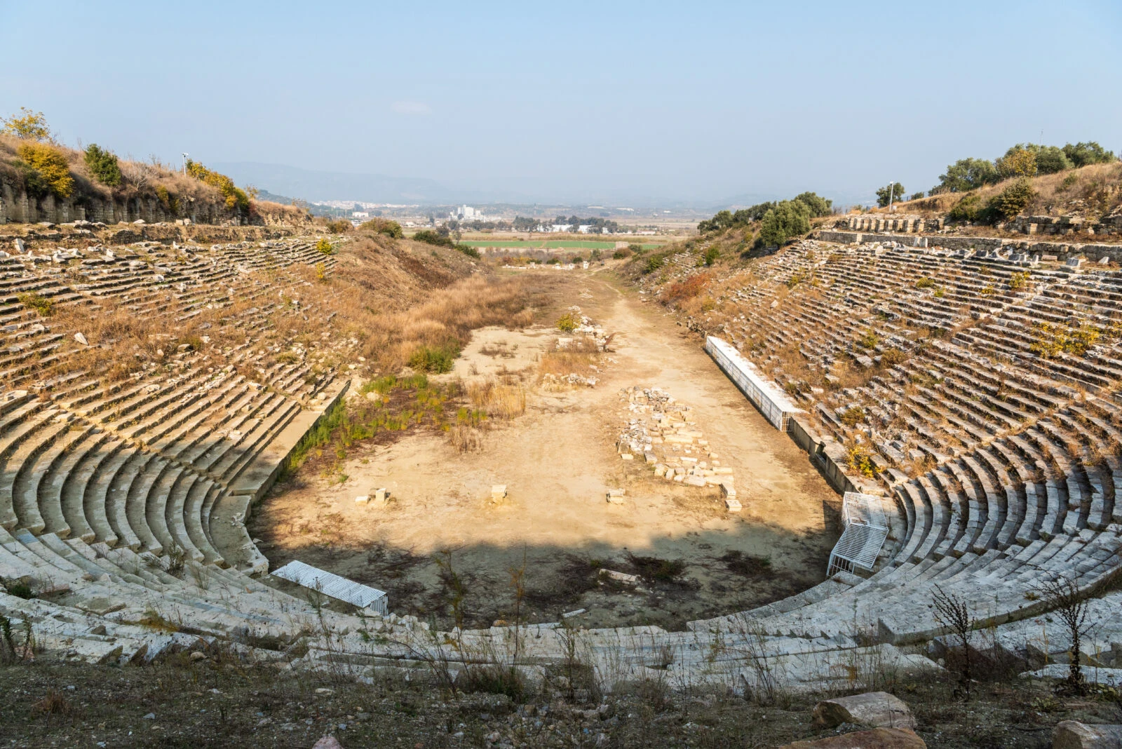 The ruins of Magnesia Stadium in Aydin, Türkiye, with stone seating visible.