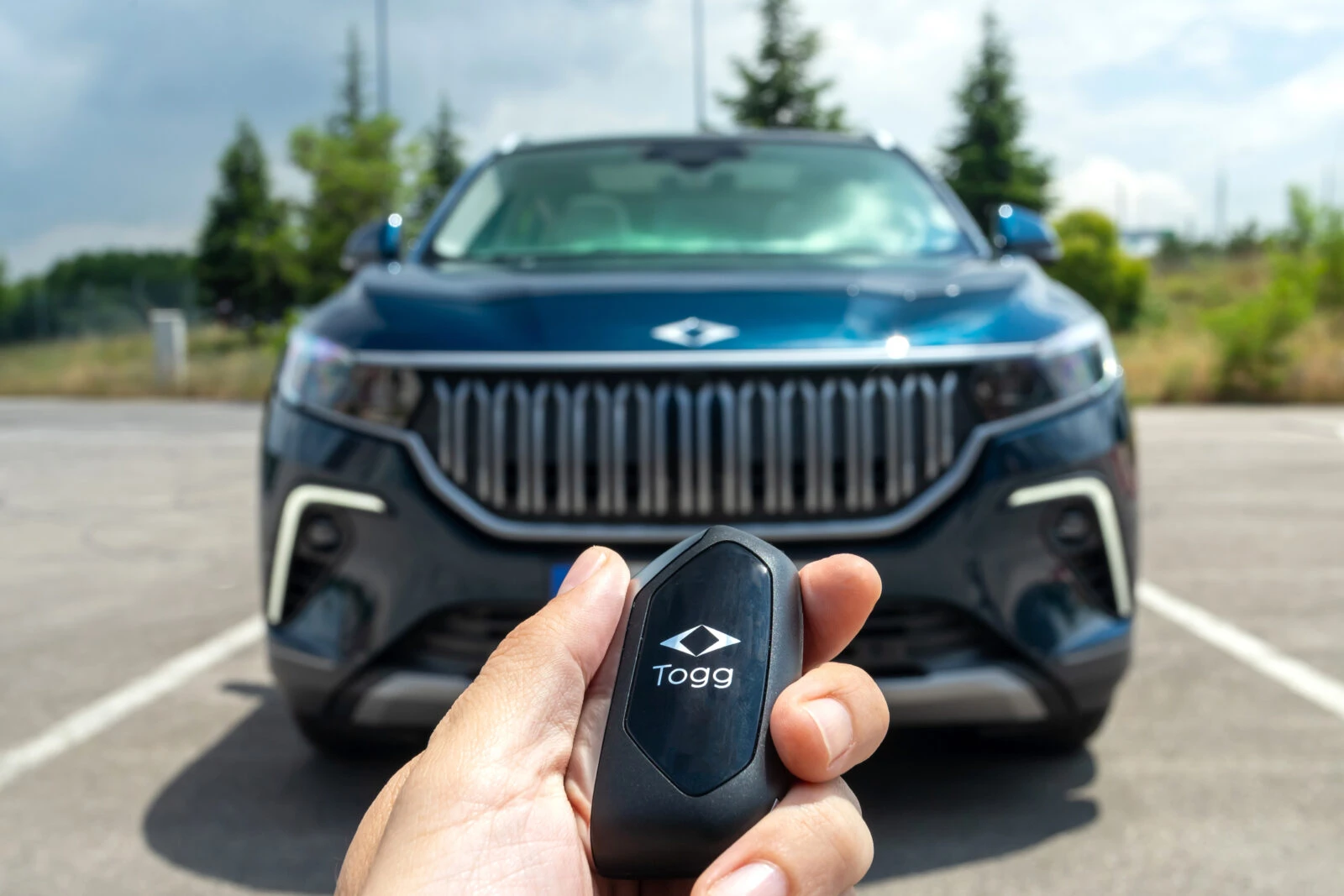 a close-up of a person holding a Togg-branded car key fob in front of a Togg electric vehicle (EV)