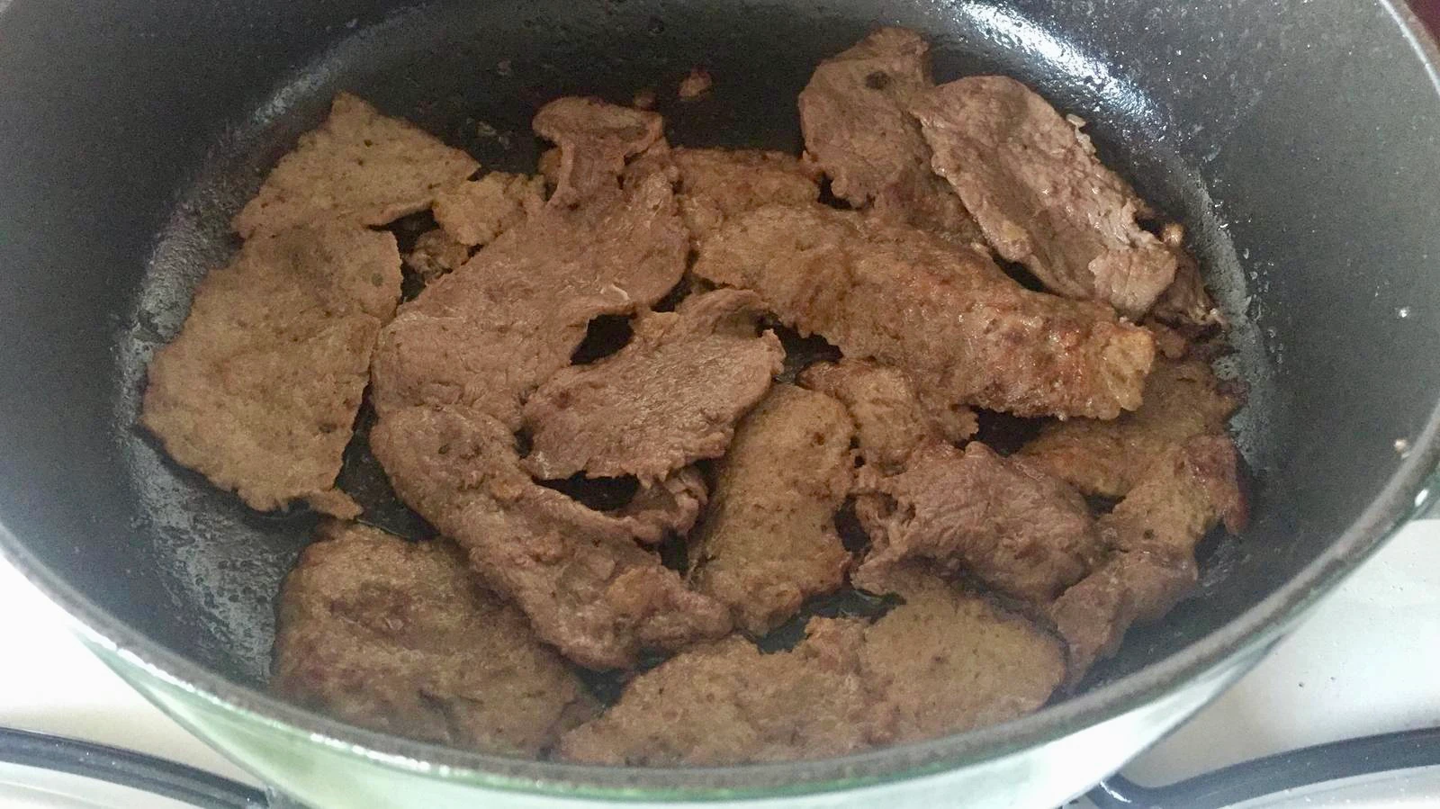 Beef slices sizzling on a pan as they cook.