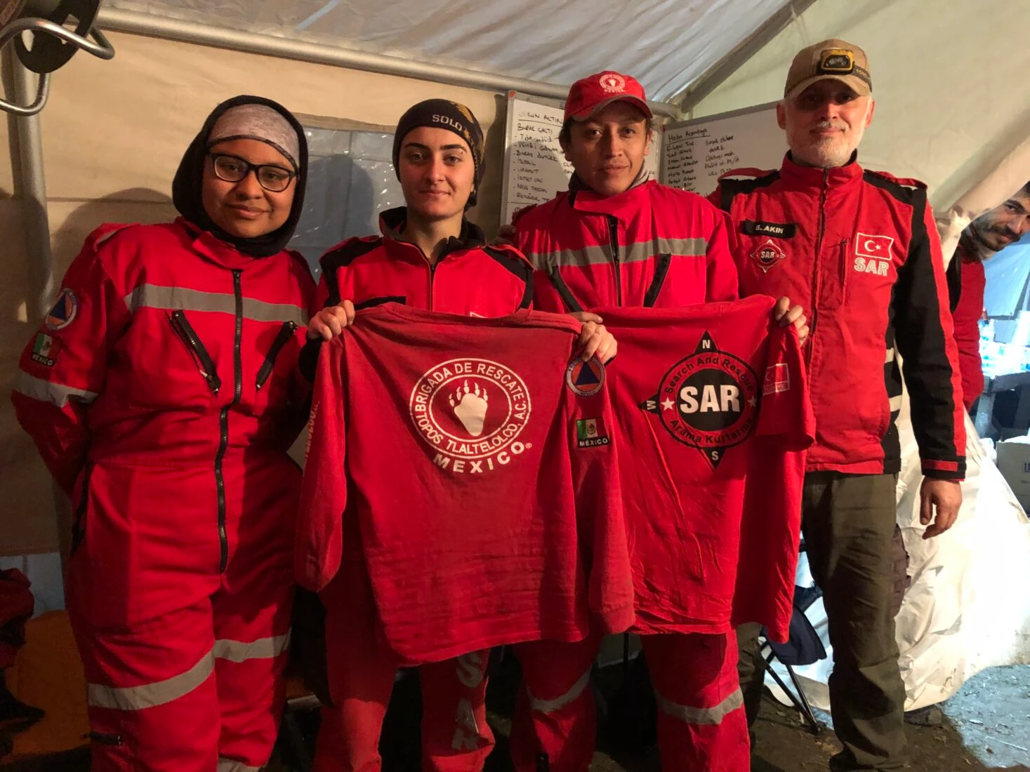 Turkish and Mexican search-and-rescue volunteers pose with exchanged team shirts inside a rescue camp