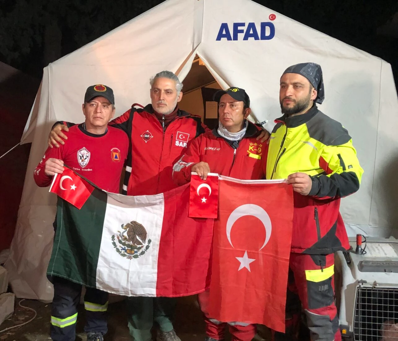 Mexican and Turkish SAR members hold their national flags in front of an AFAD tent during rescue efforts