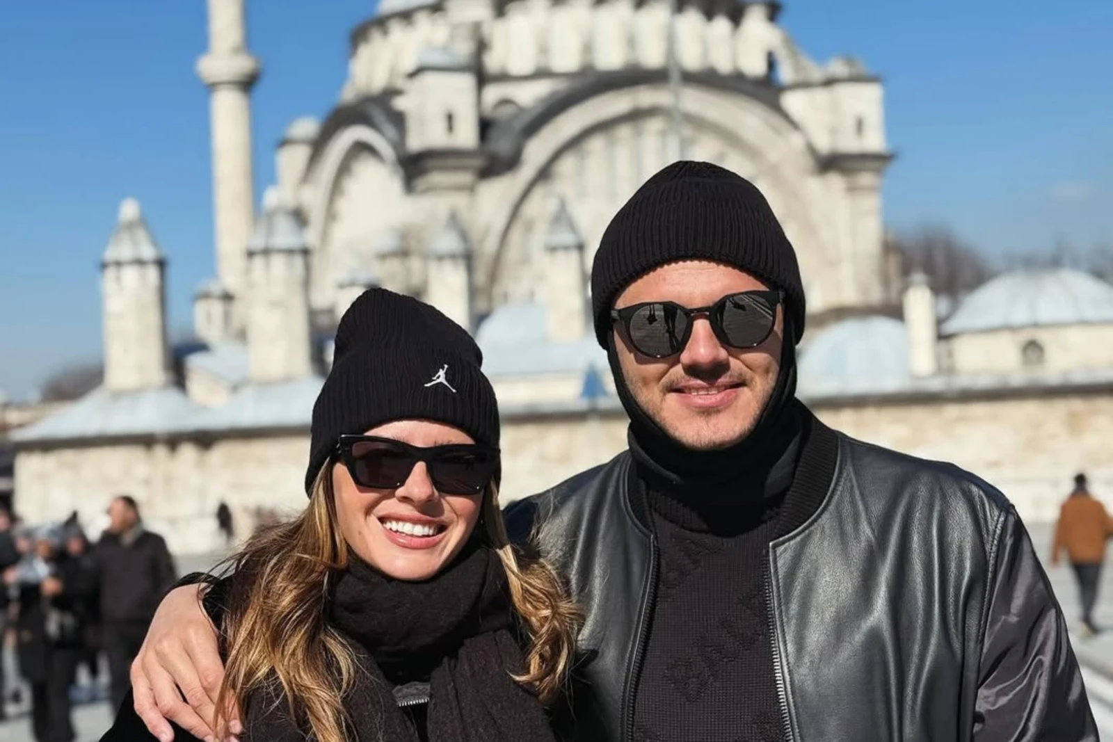 Mauro Icardi and China Suárez wearing black winter outfits, smiling in front of a historic mosque in Istanbul.