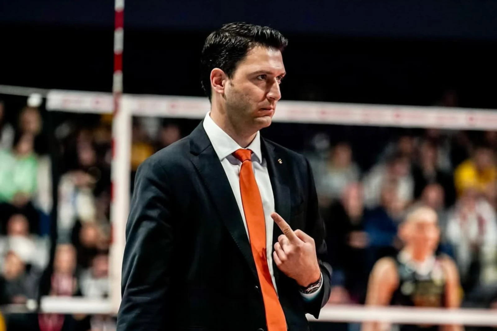 Turkish volleyball coach Ferhat Akbas wearing a black suit and orange tie, intensely directing his team during the Vakifbank Istanbul vs. Eczacibasi Vitra match on December 14, 2024