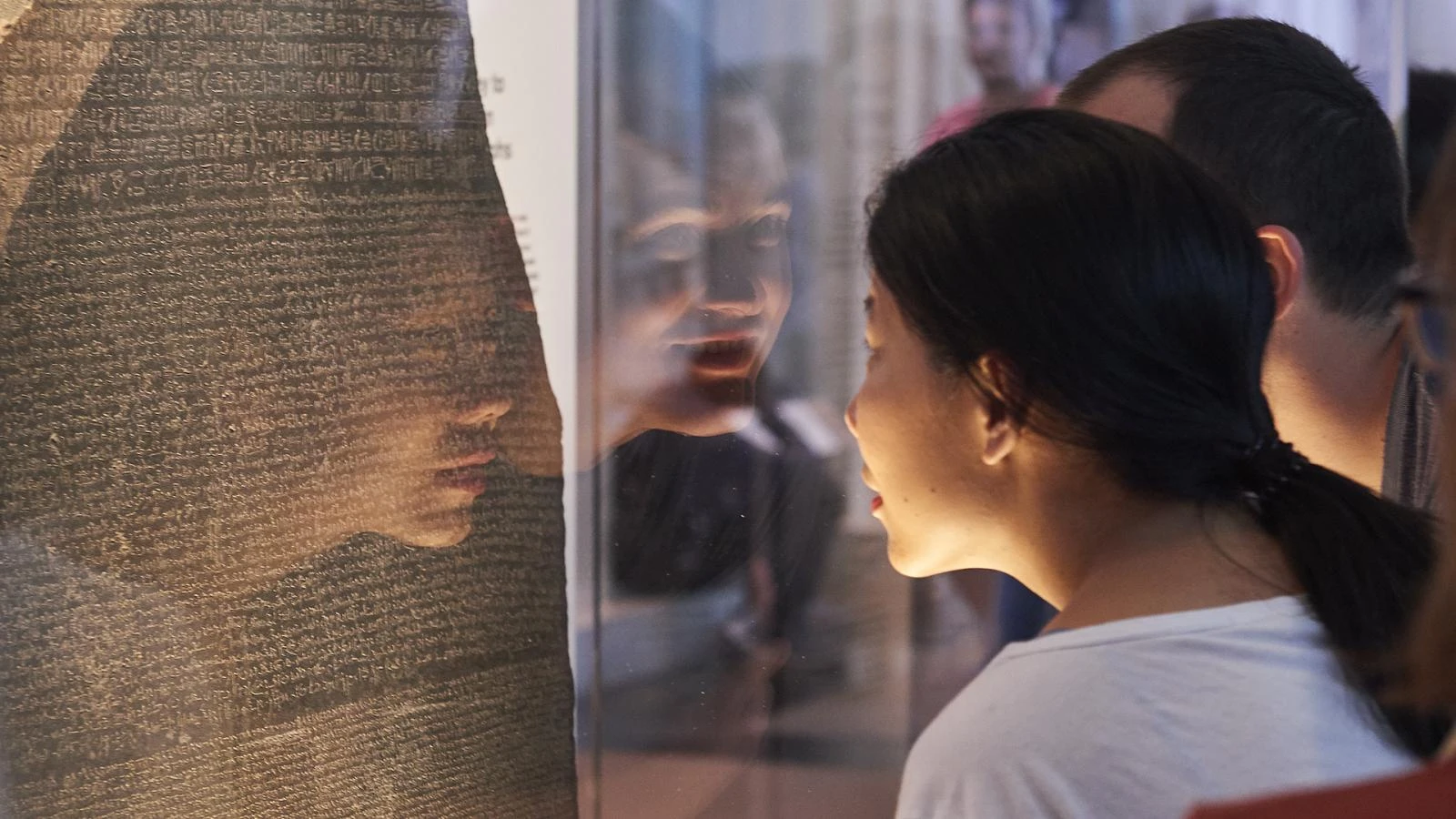 A group of visitors observing the Rosetta Stone, an ancient artifact, at the British Museum in London.