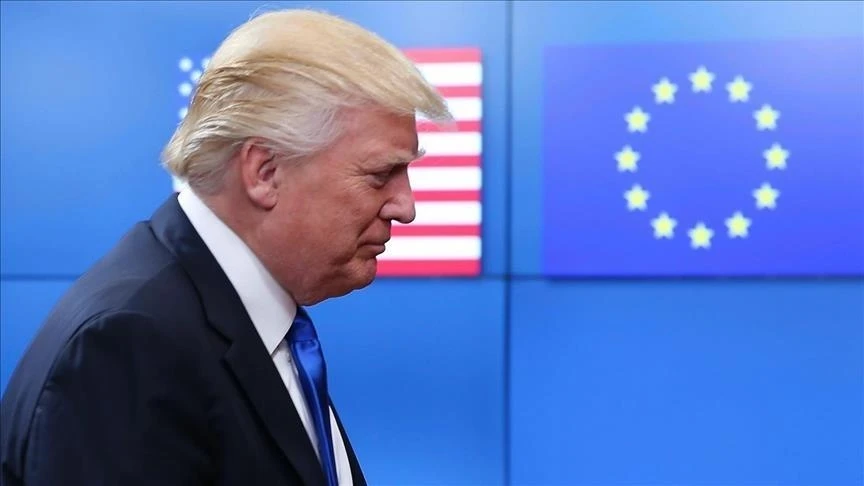 U.S. President Donald Trump walking past a backdrop featuring the flags of the U.S. and the EU