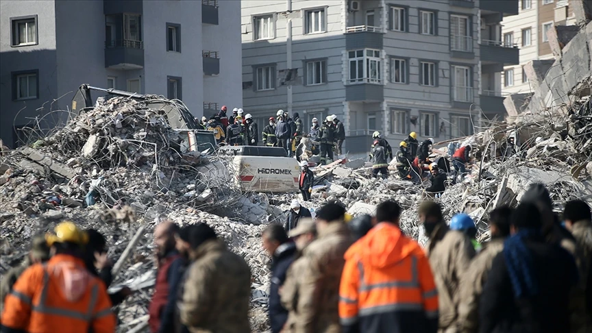 Rescuers in helmets and safety vests search through the wreckage of a collapsed building in Hatay