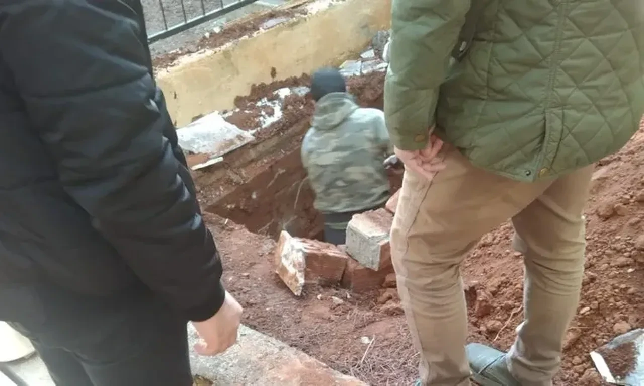 Several people, including workers and officials, observe as a man digs into a grave in Mugla, Türkiye, during the exhumation of Mustafa Uyanik for a DNA test.