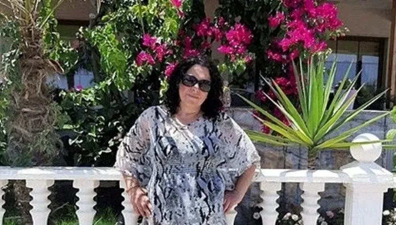 A woman wearing sunglasses and a patterned dress poses in front of a garden with blooming pink flowers, later identified as Berrin Nalci, who uncovered a decades-old family secret.