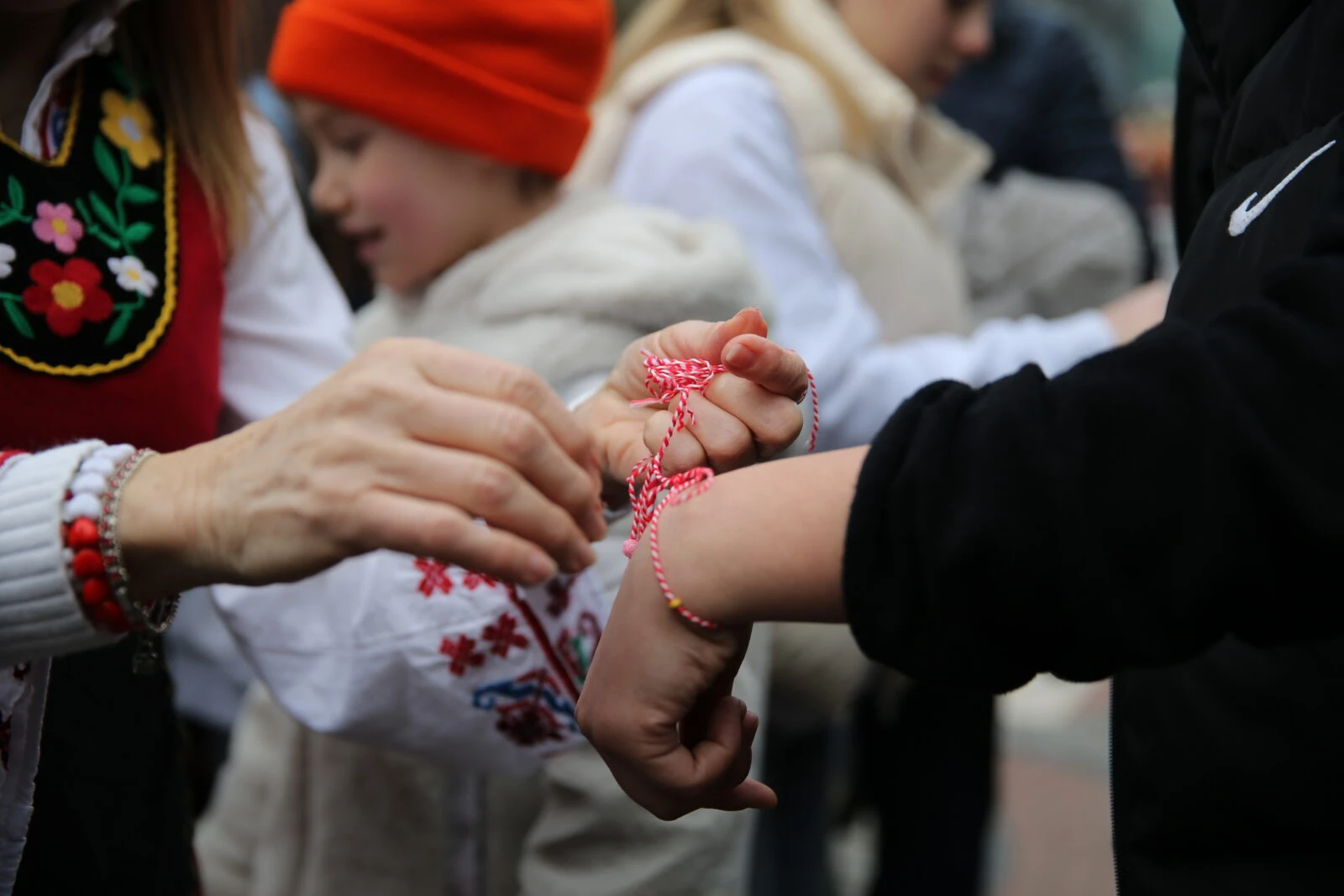 People exchanging martenitsa bracelets by tying them on each other's wrists in Edirne, Türkiye.