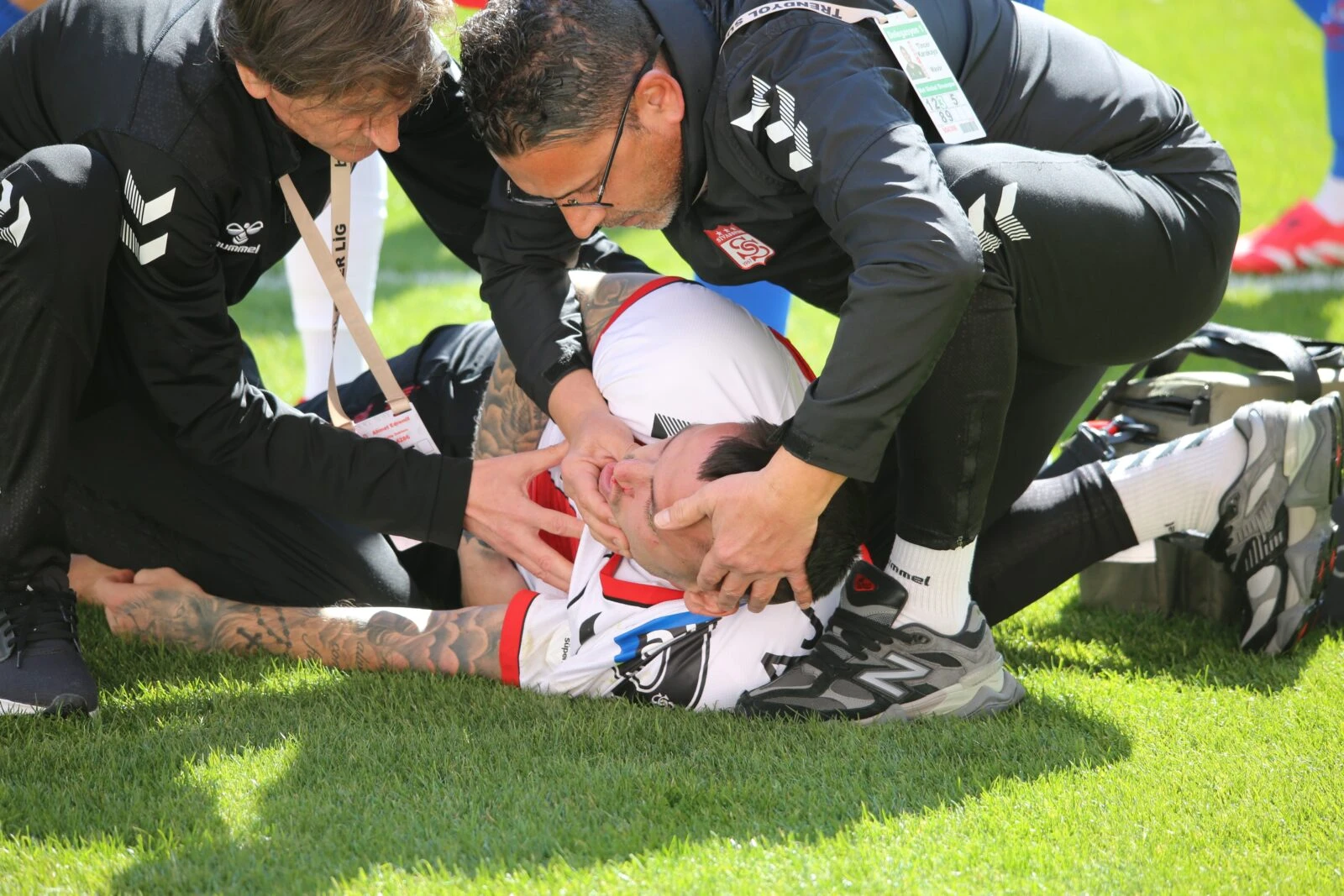 A football player lies on the field receiving medical attention from two team staff members