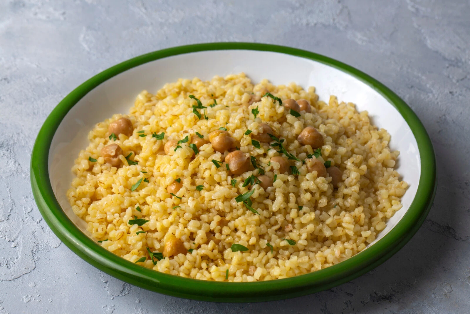 break fast - A bowl of bulgur pilaf with chickpeas, garnished with fresh herbs and served in a green-rimmed dish.