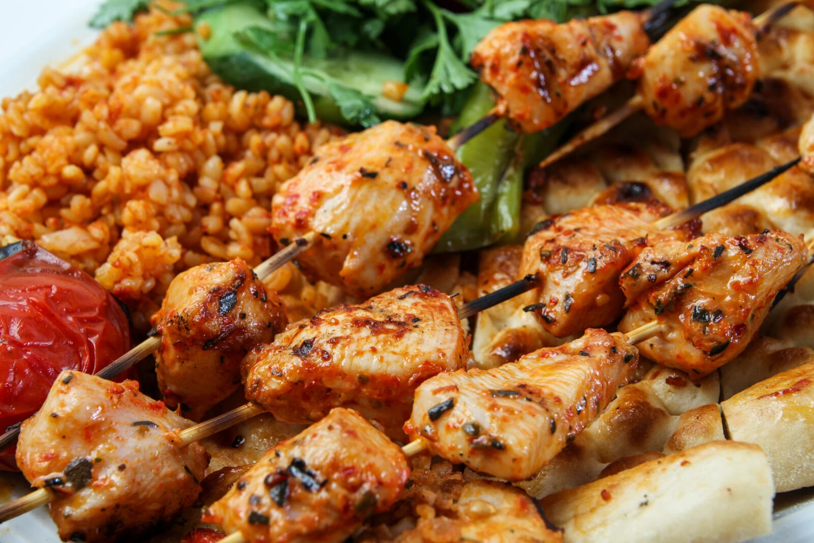 A close-up of Turkish-style grilled chicken skewers, marinated and cooked to perfection, served with bulgur pilaf, grilled tomatoes, and peppers.