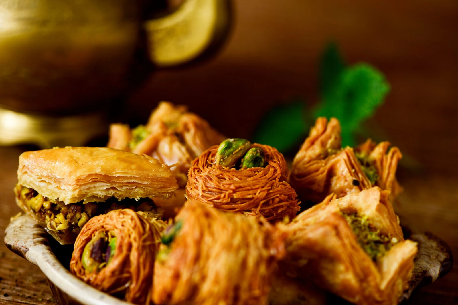 A plate of assorted pistachio and almond-filled pastries, including baklava and kataifi, arranged on a rustic wooden surface.