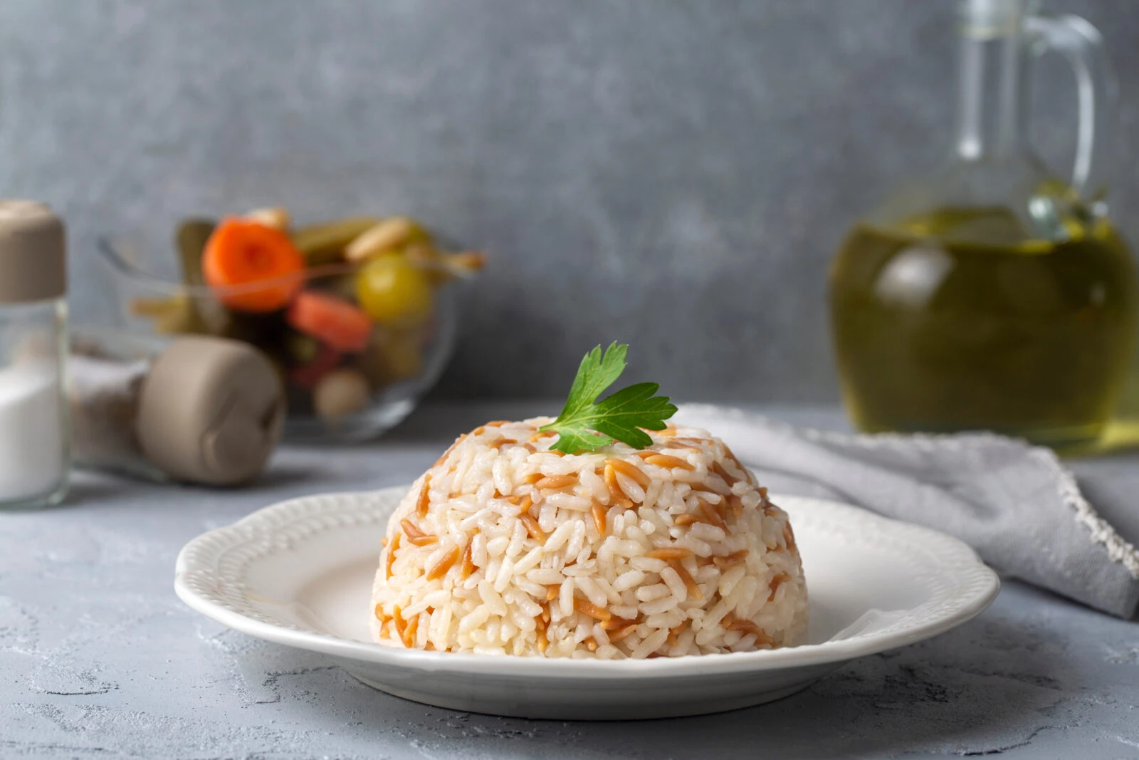 A serving of Turkish orzo and butter pilaf, known as arpa sehriyeli pilav, plated with a sprig of parsley and set against a traditional dining backdrop.