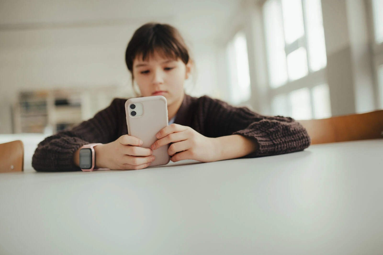 Young schoolgirl sitting in a science lab with a phone in her hand, waiting for classmates. (Adobe Stock Photo)