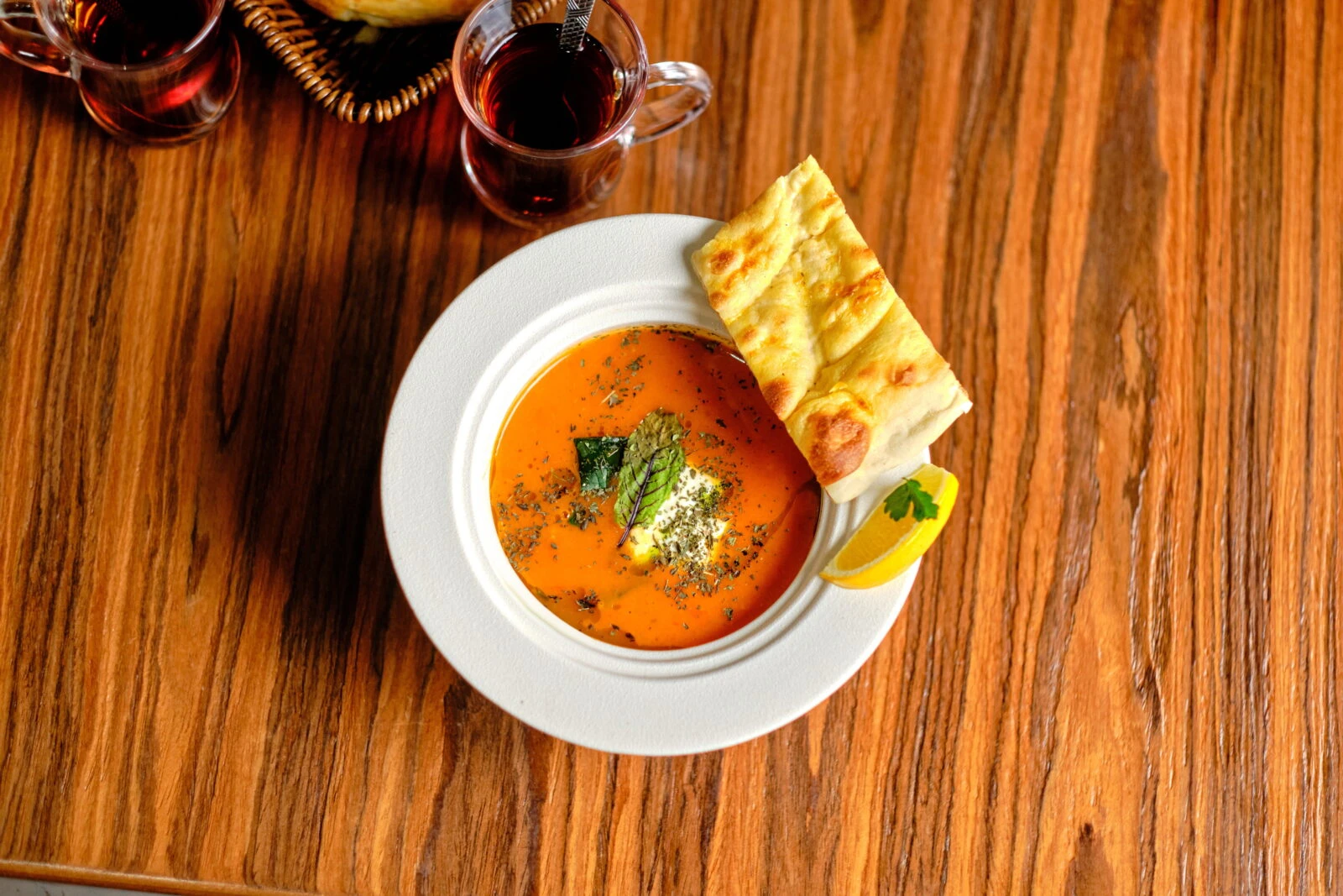 A bowl of tarhana soup, a Turkish fermented soup with a creamy texture, served with pita bread, tea, and lemon on a wooden table.