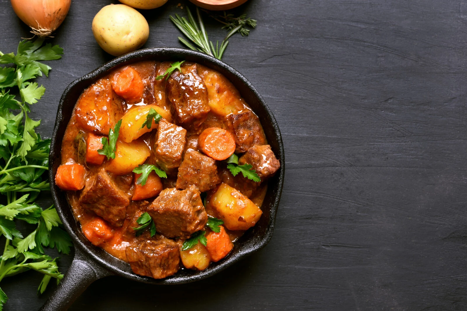 A cast-iron skillet filled with Turkish lamb stew, featuring potatoes, carrots, and herbs.