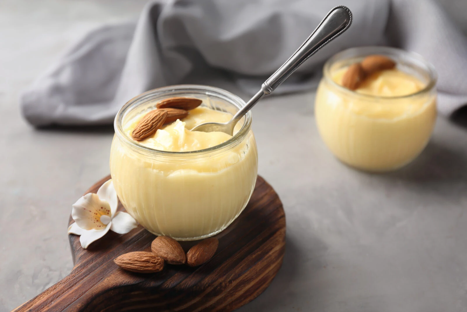 A close-up of a glass jar filled with smooth almond pudding, topped with whole almonds, placed on a rustic wooden surface.