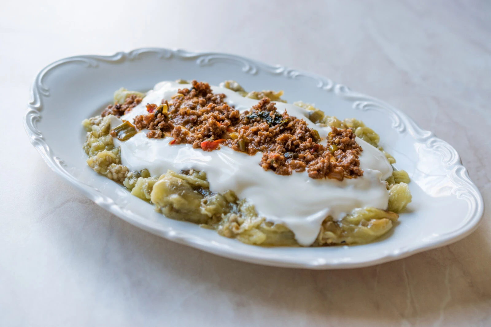 A plate of Turkish eggplant and yogurt dip, topped with a spiced minced meat mixture, served on a white decorative dish.