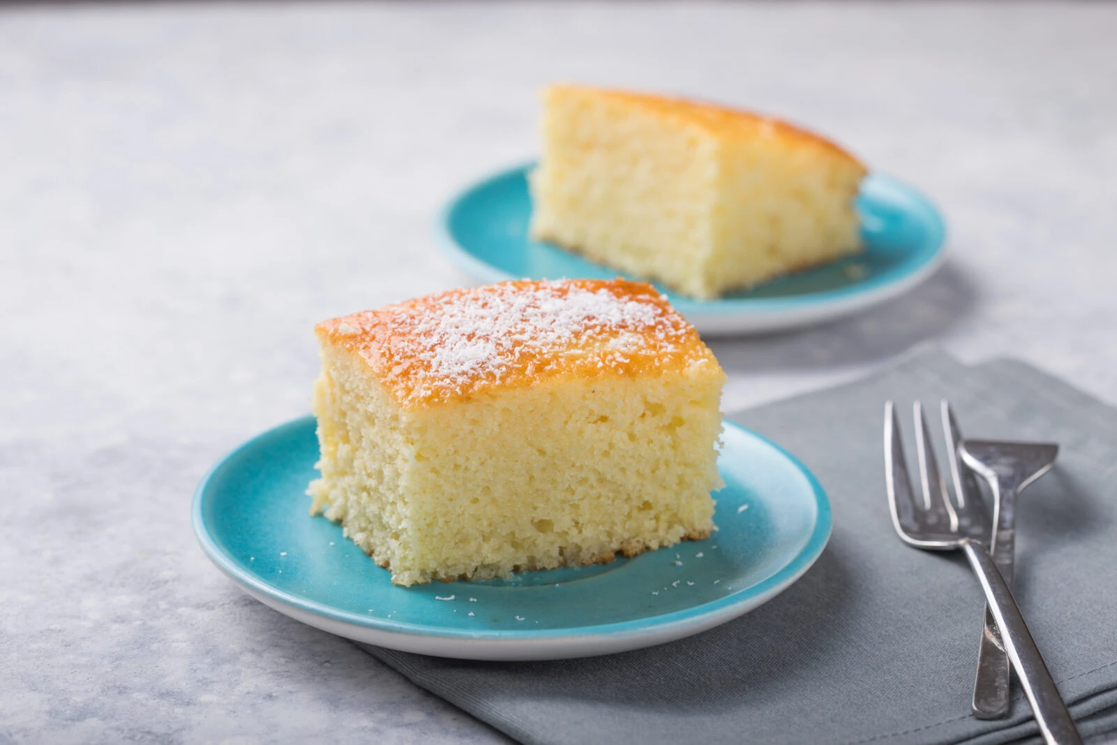 Two slices of Turkish revani cake on blue plates, topped with coconut flakes, a classic dessert enjoyed after iftar.