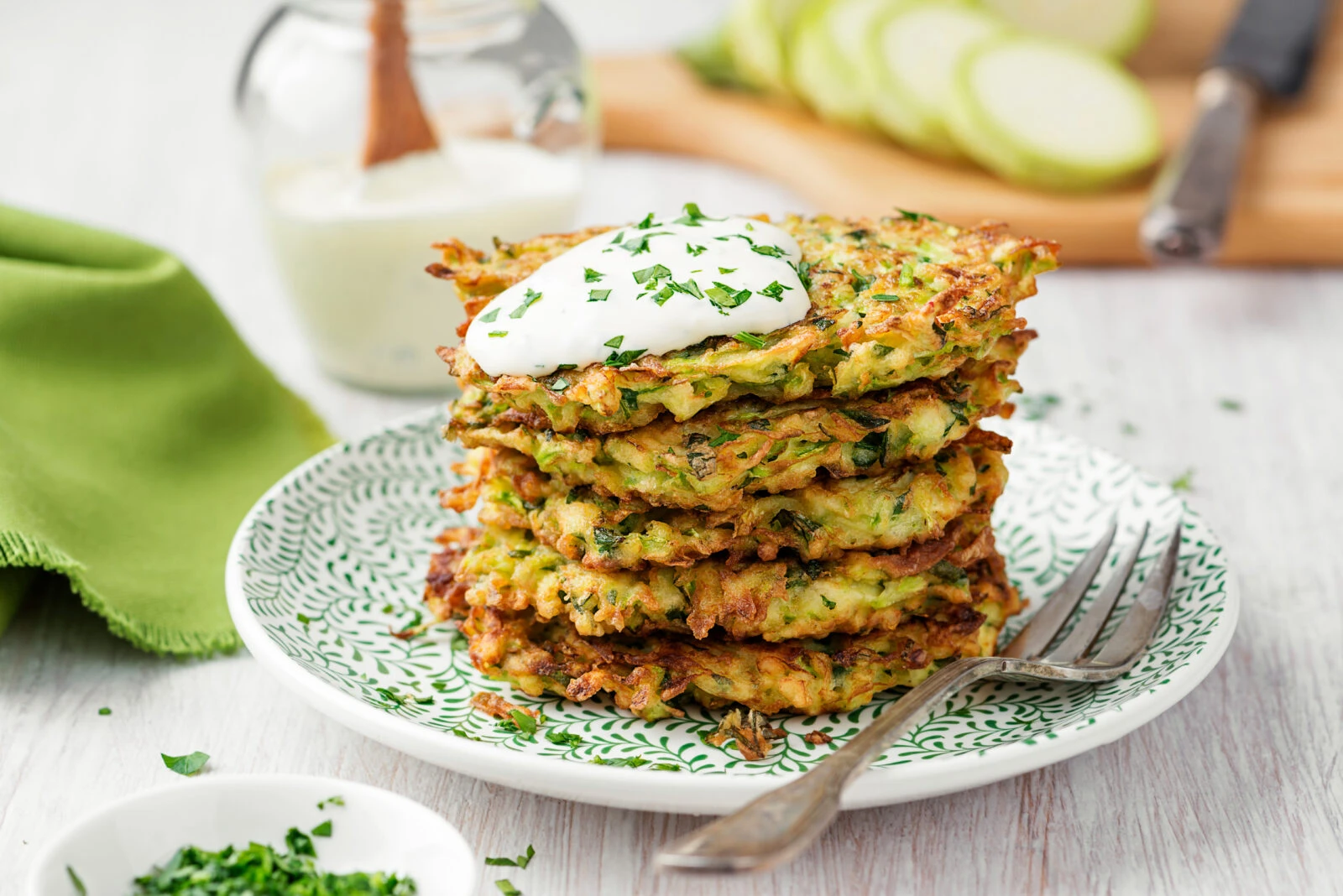 A stack of golden-brown Turkish zucchini fritters (mucver) topped with yogurt and sprinkled with chopped parsley.