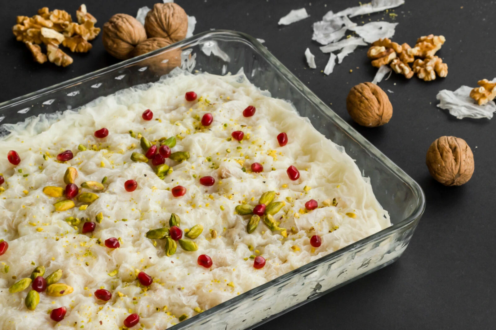 Traditional Turkish gullac dessert in a glass container with walnuts on a black background.