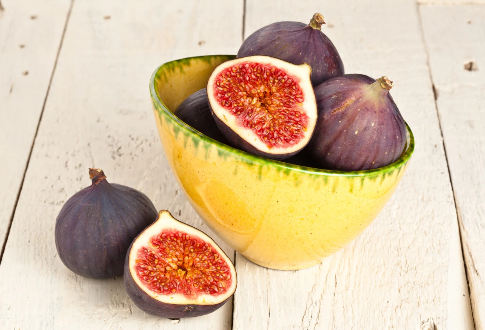 Bowl with Bursa's black figs, with some figs sliced open to reveal their red interior, placed on a wooden surface.