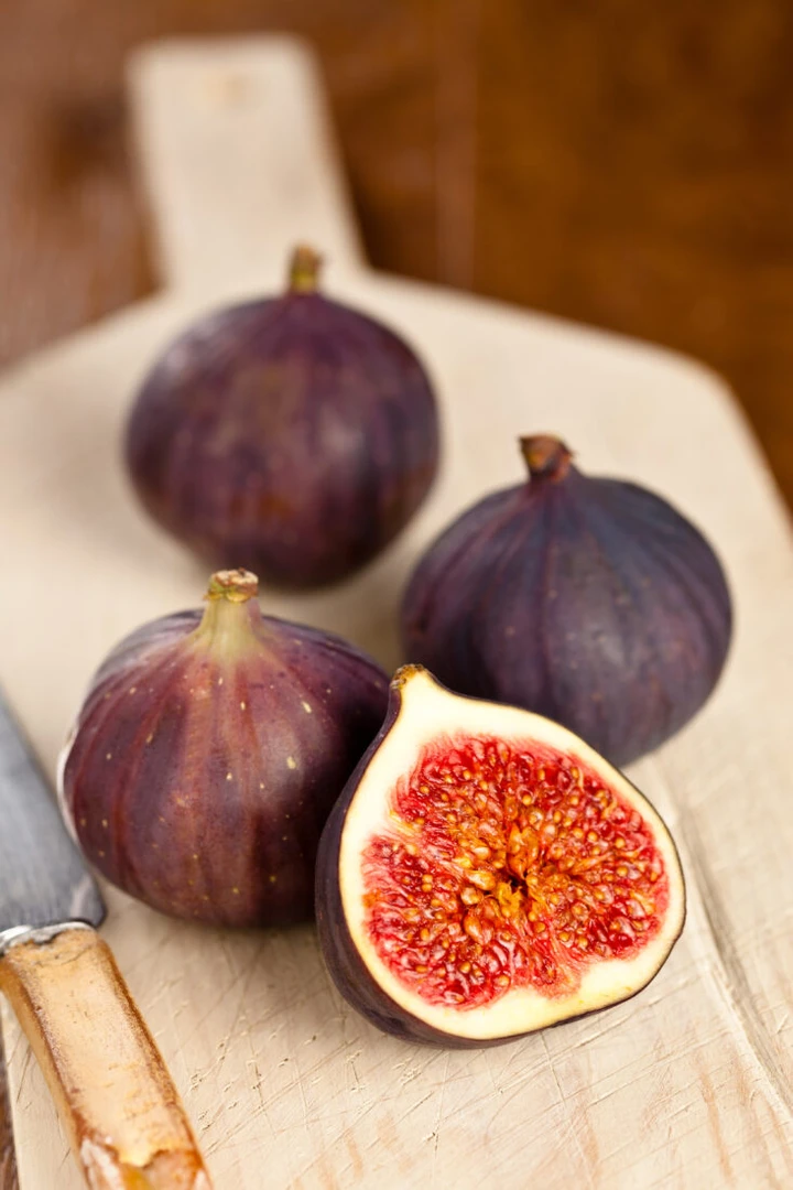 Whole and sliced black figs on a wooden board, showcasing their dark purple skin and red interior.