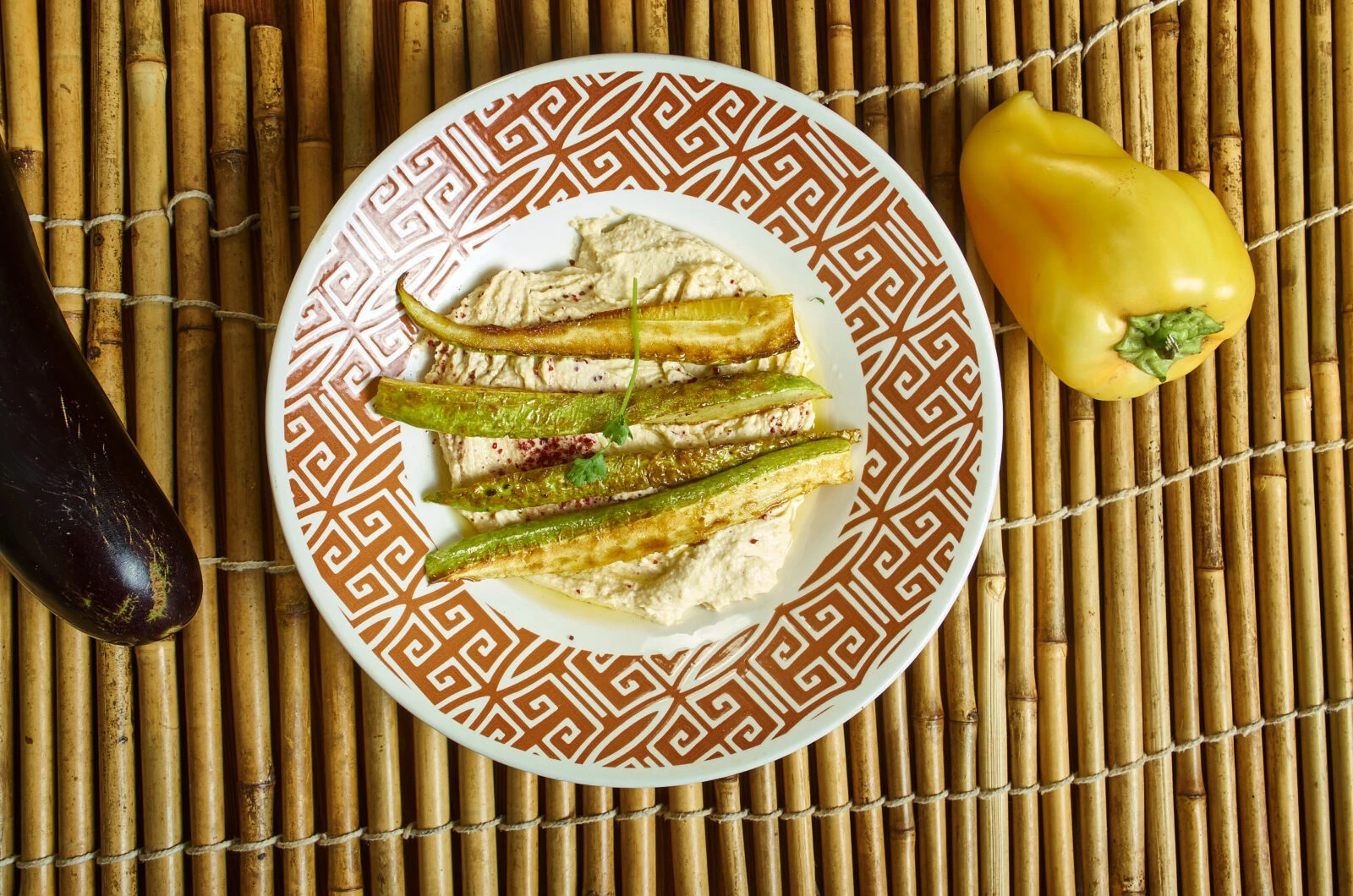 A plate of oven-roasted zucchini strips over a tahini-based dip, served on a patterned plate with fresh herbs.