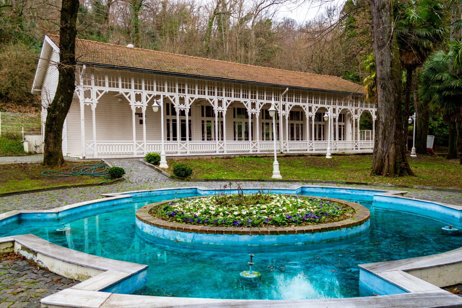 A traditional wooden pavilion with white latticework, surrounded by lush greenery and a blue fountain in Yalova’s thermal springs area.