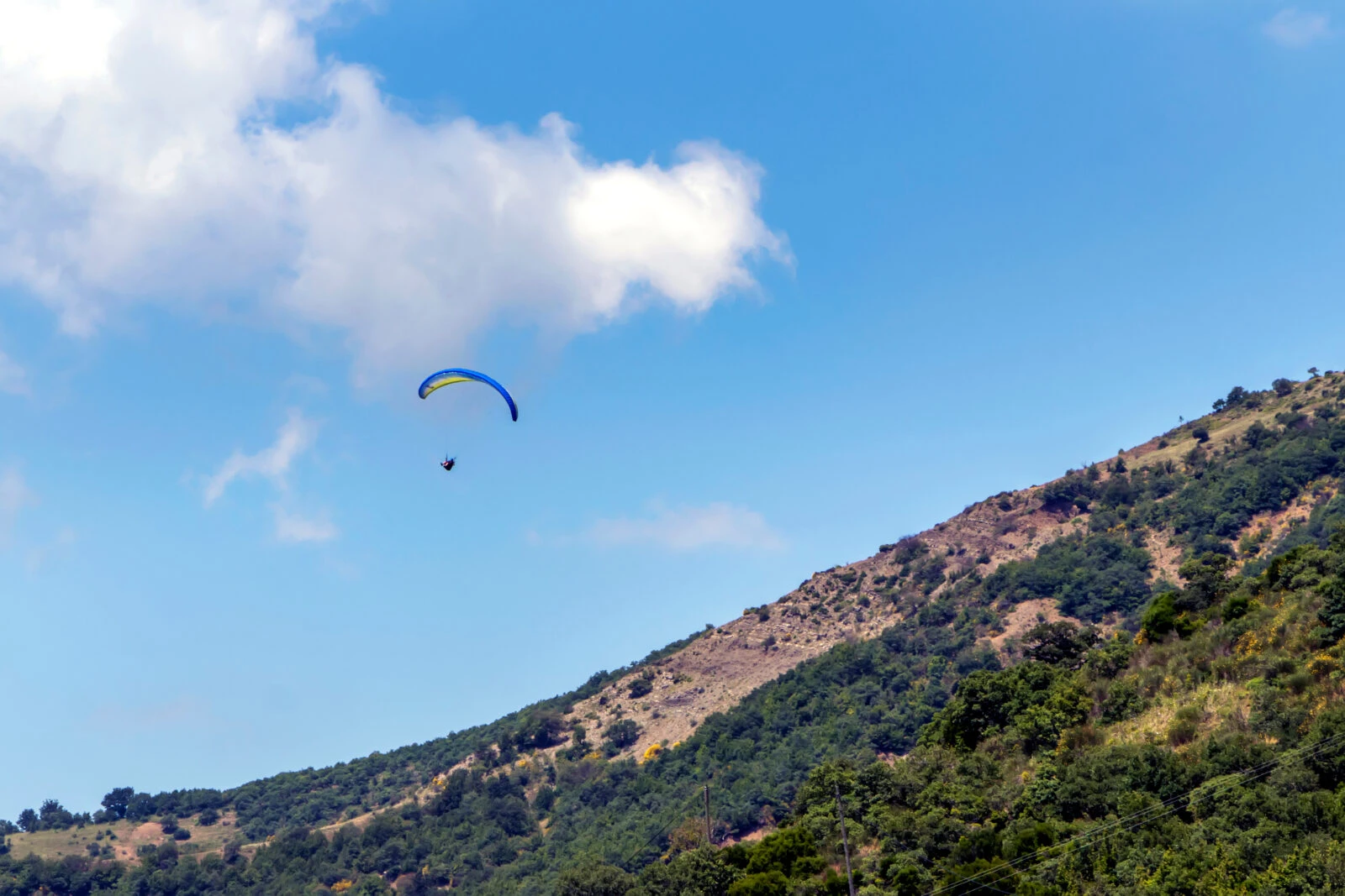 A lone paraglider in a bright blue sky above the green hills of Ucmakdere, a top paragliding spot in Tekirdag province.