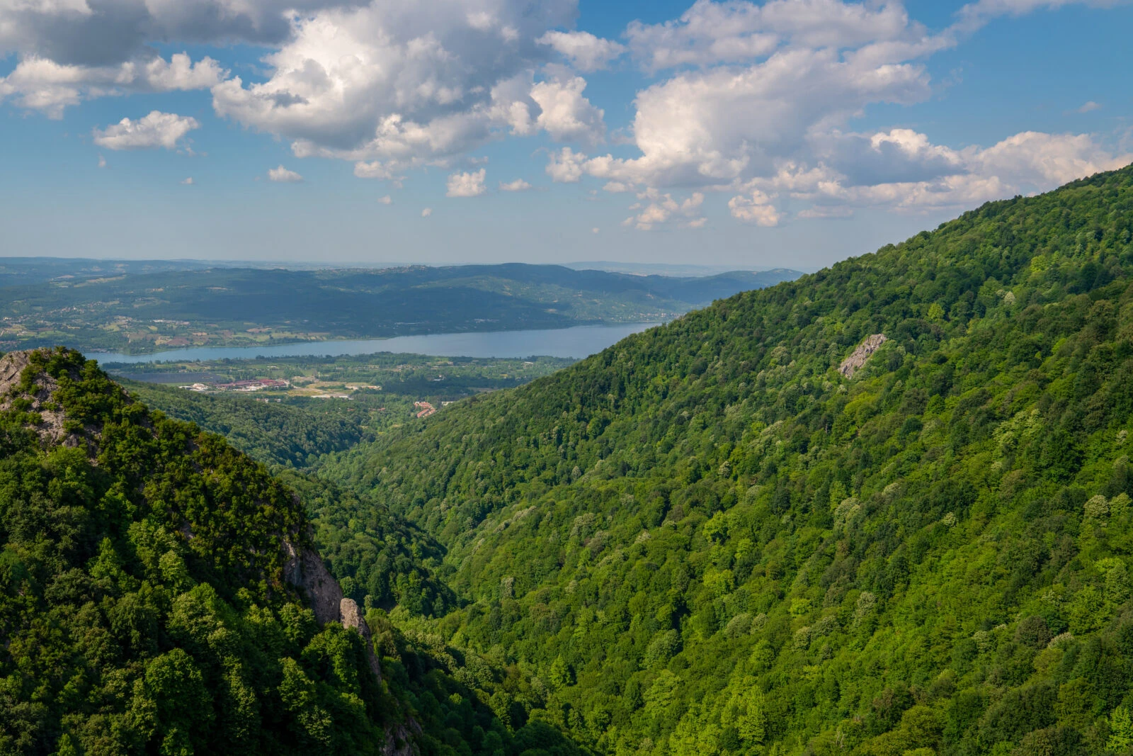 A panoramic view of Kartepe’s forested slopes, overlooking the blue waters of Sapanca Lake, under a partly cloudy sky.