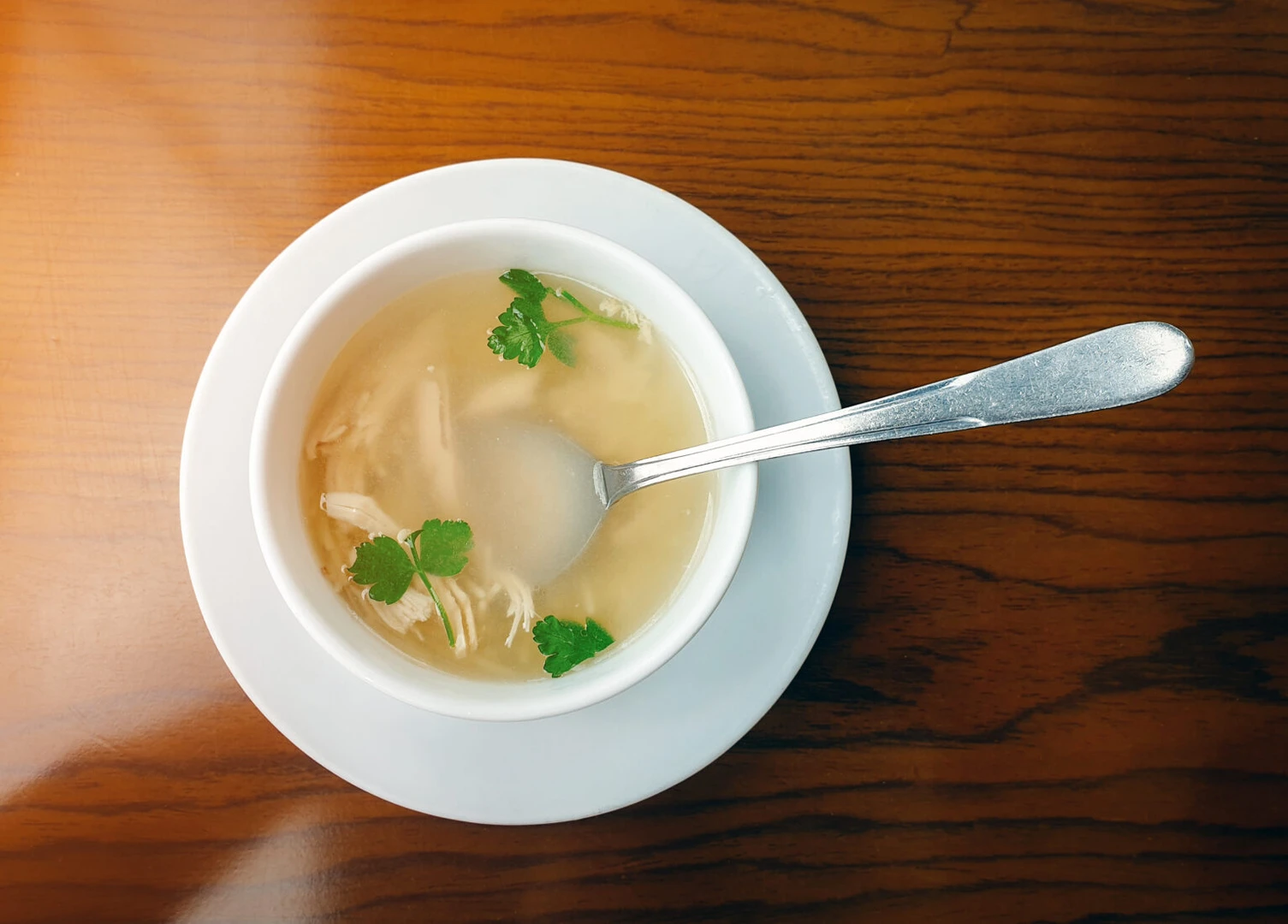 iftar soup, A white bowl of creamy chicken and vermicelli soup with shredded chicken and fresh parsley, placed on a wooden table with a silver spoon resting inside.