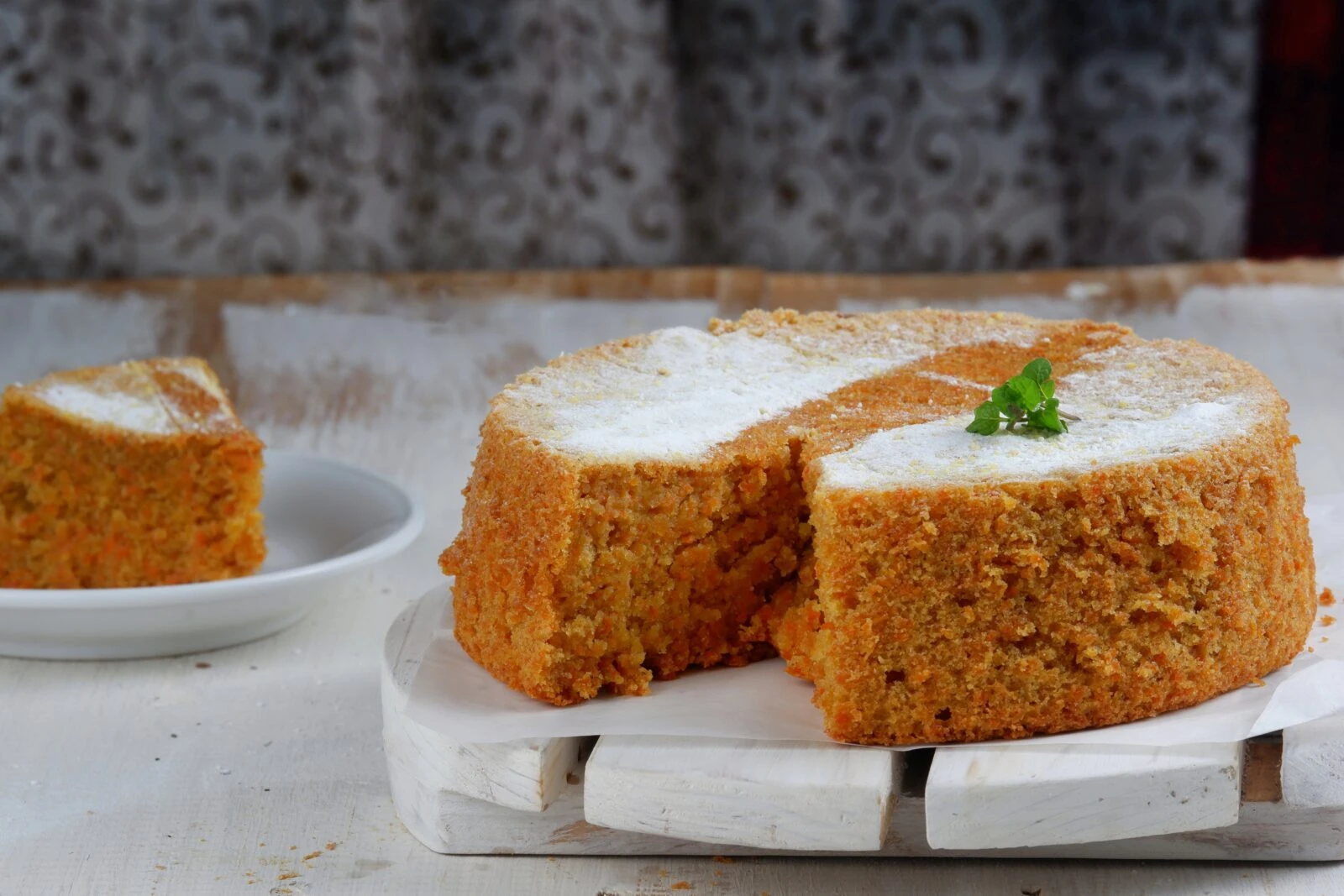 A freshly baked Turkish-style carrot and cinnamon cake with a soft, golden texture, garnished with powdered sugar and a mint leaf.