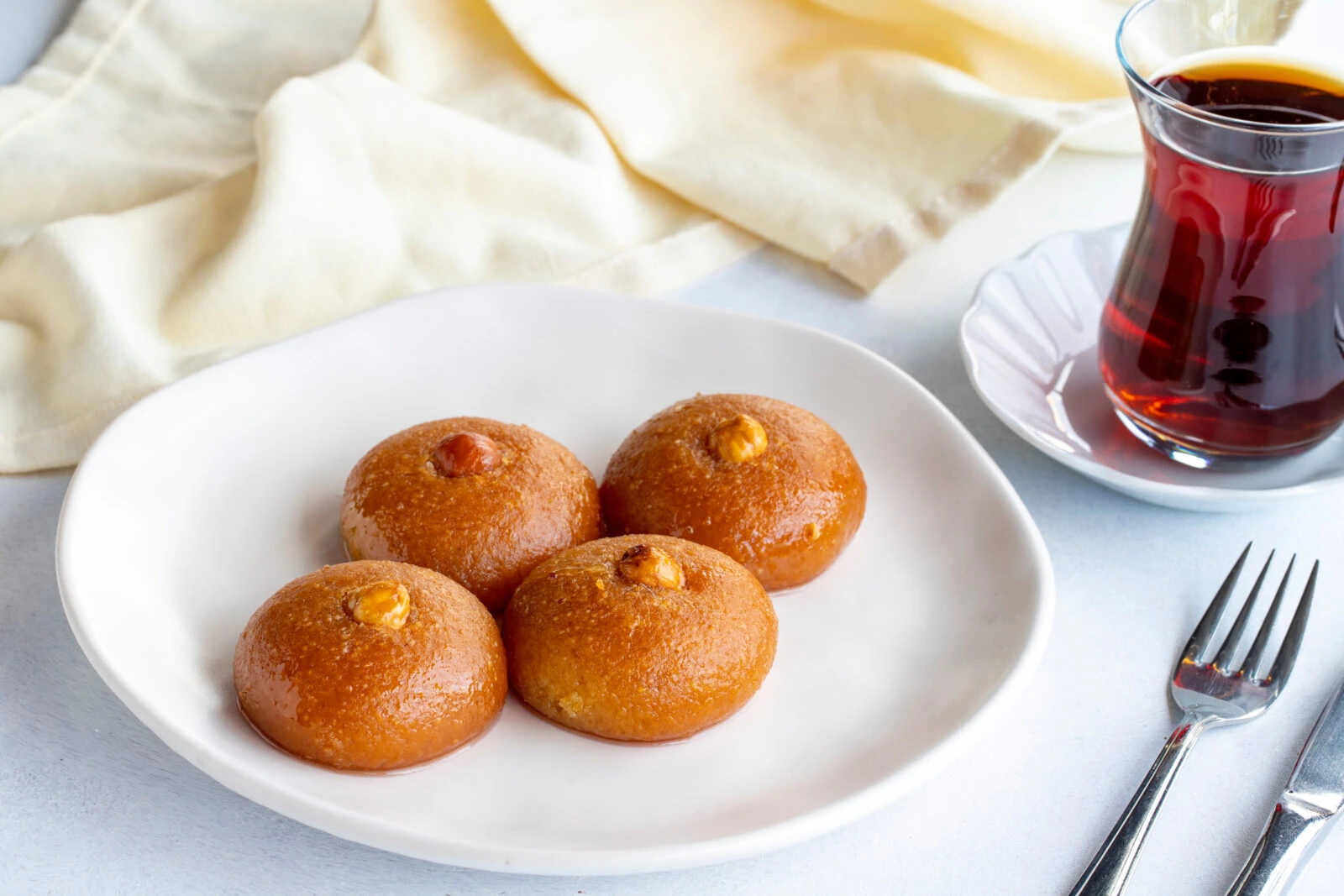 A plate of Turkish sekerpare, golden-brown semolina cookies topped with hazelnuts and soaked in sweet syrup, accompanied by tea.