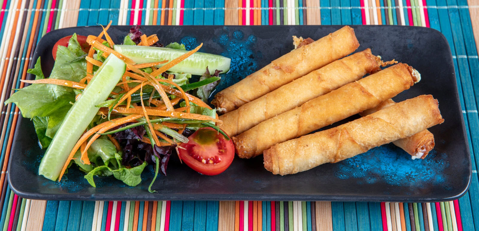 Turkish cuisine appetizer - A plate of golden-brown sigara boregi, Turkish recipe cheese and parsley-filled pastry rolls, served with a side salad including cucumber, tomatoes, and shredded carrots.