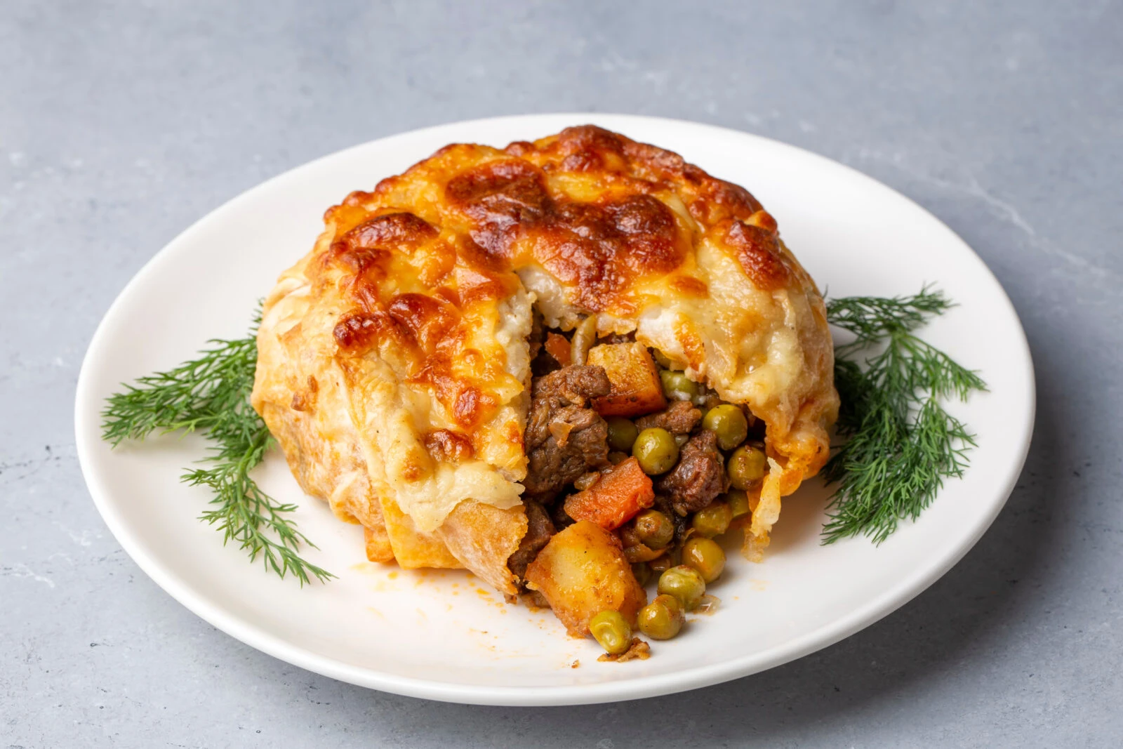 A golden-baked Turkish bohça kebabı, filled with beef, peas, and carrots, with a crispy, cheesy crust on top.