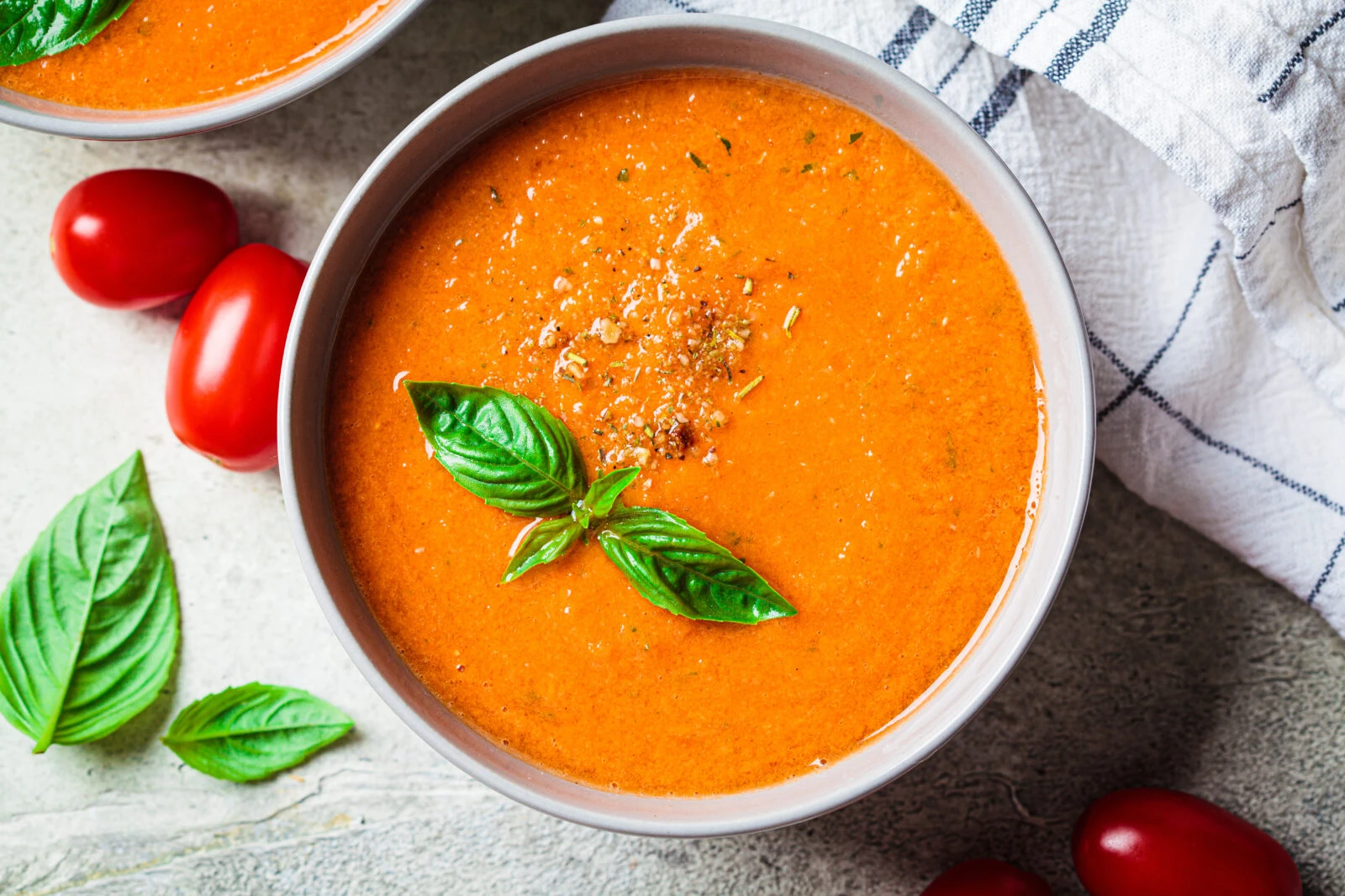 A steaming bowl of Turkish-style tomato soup topped with fresh basil, served alongside ripe tomatoes and herbs.