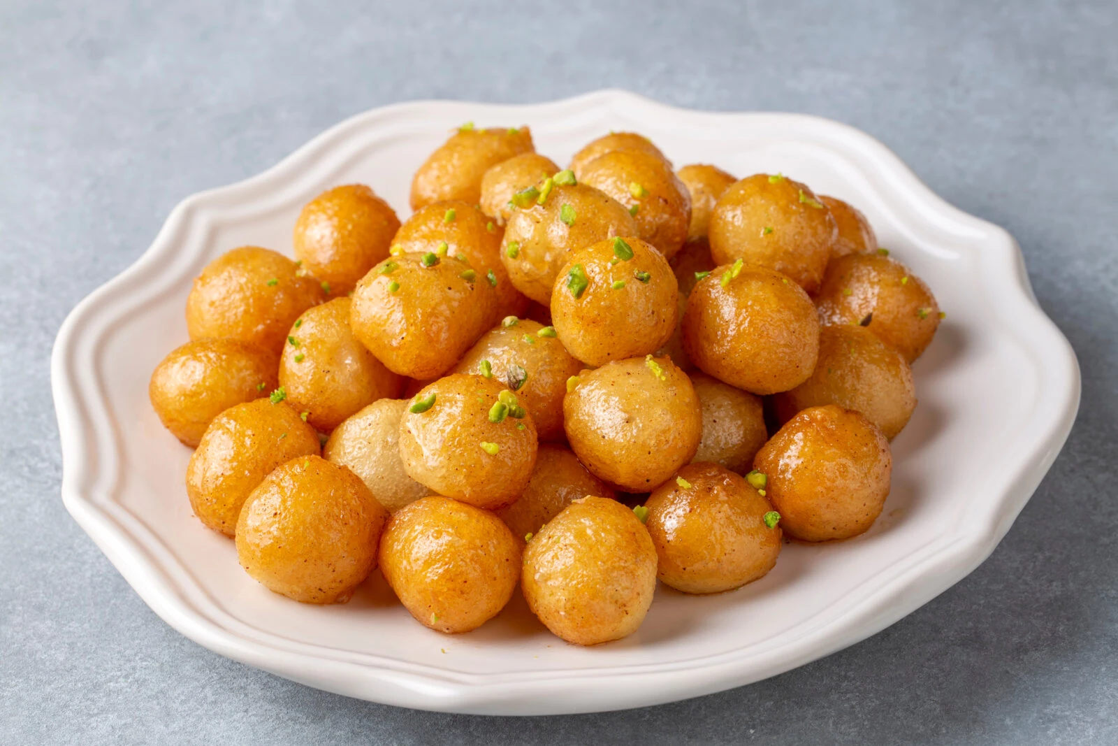 A plate of round, deep-fried lokma soaked in syrup, garnished with crushed pistachios.