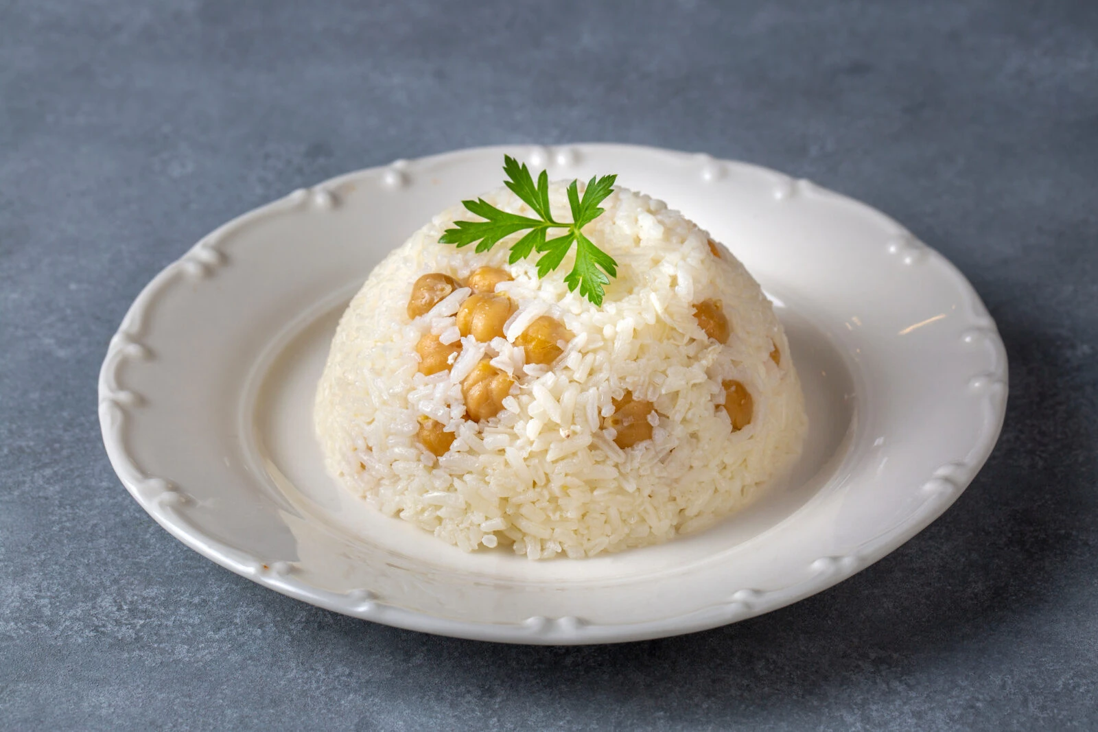 A plate of Turkish chickpea rice pilaf, known as Nohutlu Pilav, garnished with fresh parsley and served on a white plate.